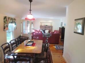 A dining area with a wooden table and chairs, a red sofa, and a hanging light fixture. - Chatham Ranch Retreat Near Hardings Beach (Chatham)