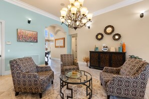 A living room with patterned armchairs, a glass coffee table, and a chandelier.