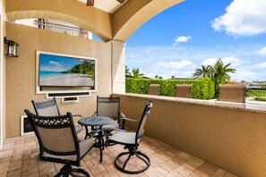 A balcony with a TV, outdoor furniture, and a view of a beach.