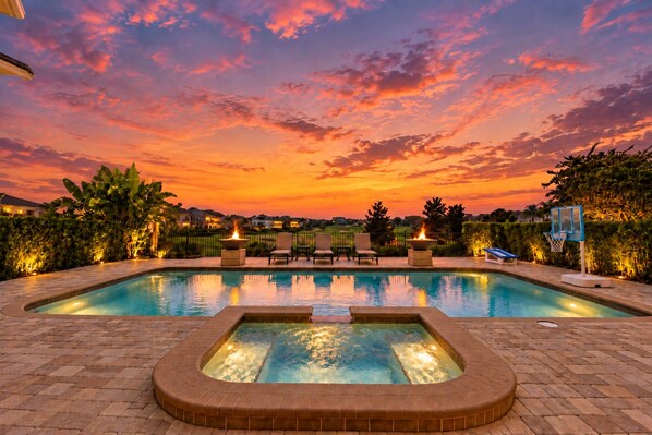 A swimming pool with a hot tub, lounge chairs, and a basketball hoop.