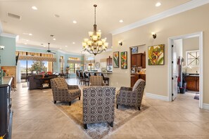 A spacious living area with a chandelier, patterned armchairs, and a dining area with bar stools.