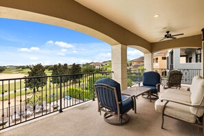 A balcony with outdoor furniture, a view of a golf course, and a building in the background.