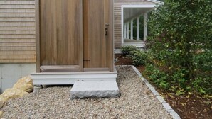 Une maison avec une porte de garage en bois, un porche couvert et une all ée gravillonnée.