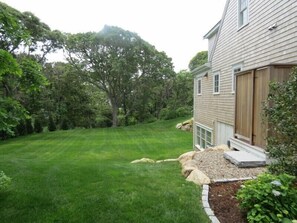 A residential property with a well-maintained lawn, a large tree, and a house with a wooden deck and a garage.