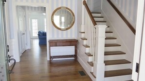 Un couloir avec un escalier, un grand miroir rond et un canapé bleu à l’arrière-plan.