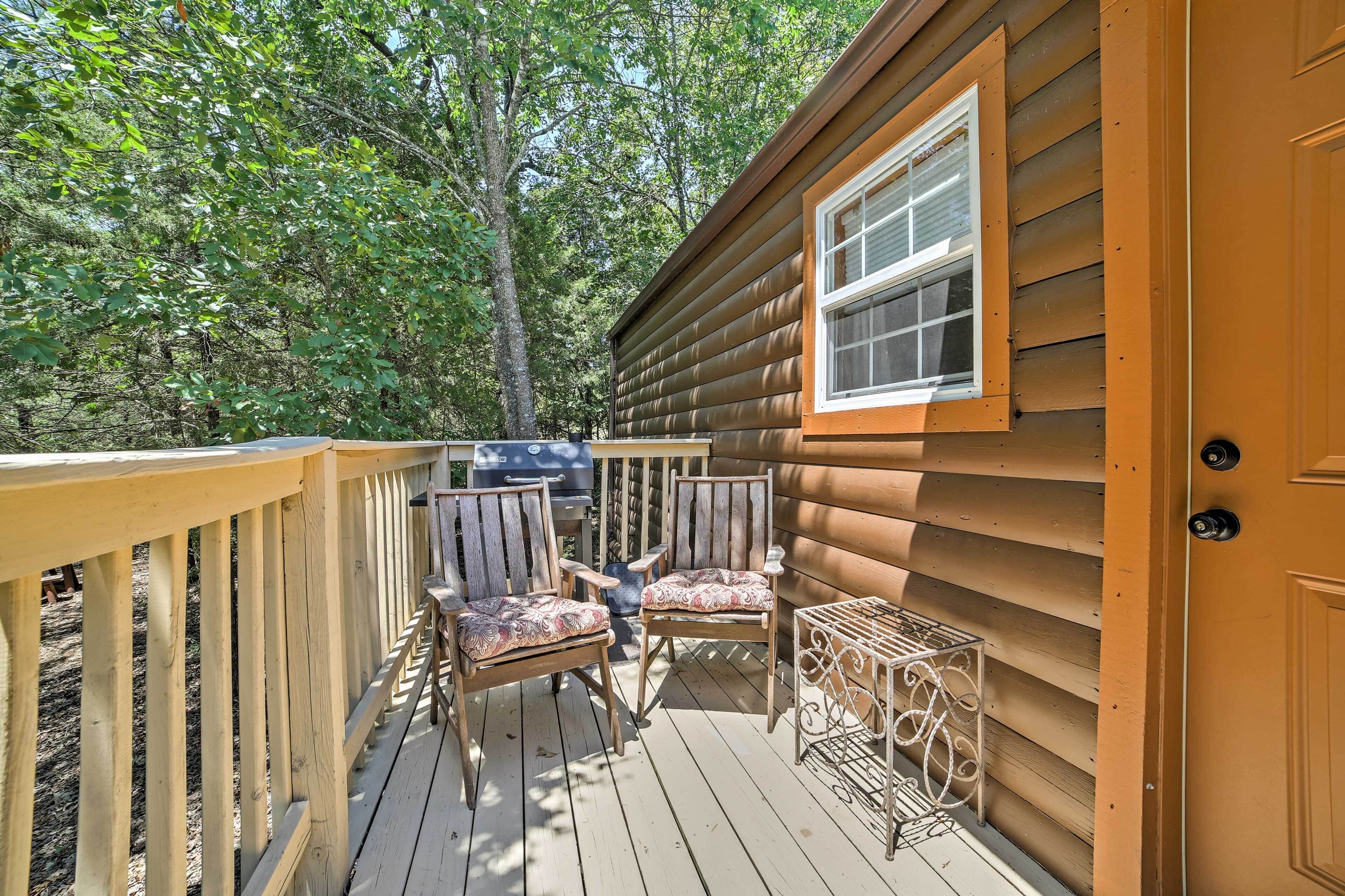 A wooden deck with two chairs and a small table, surrounded by trees.
