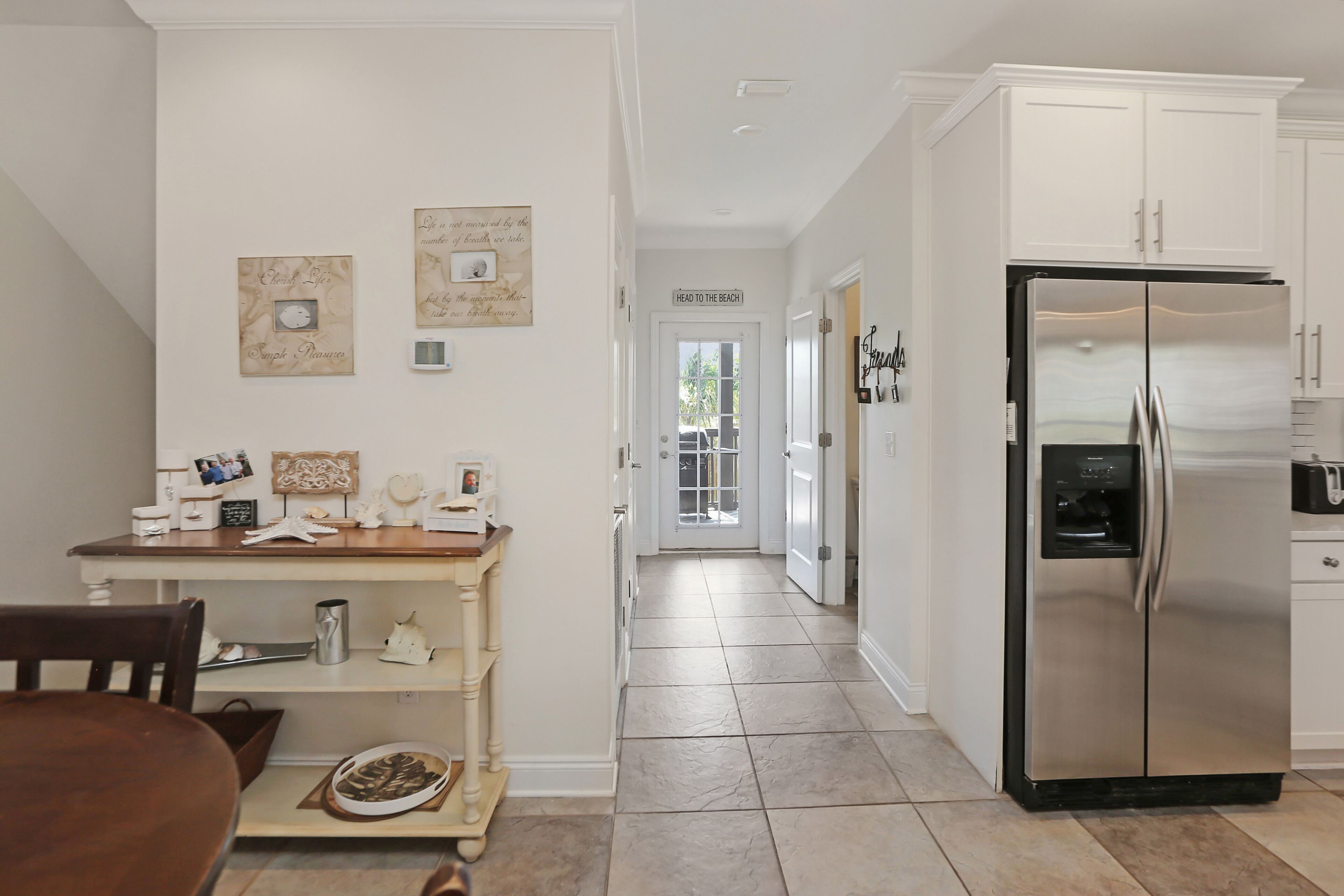 A kitchen with white cabinets, a stainless steel refrigerator, and a dining area with a wooden table and chairs.