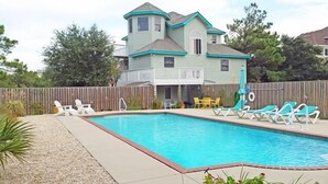 Ein zweigeschossiges Haus mit Swimmingpool, umgeben von einem Holzzaun und verschiedenen Gartenmöbeln.