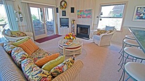 Ein Wohnzimmer mit einer Couch, einem runden Couchtisch mit Blumen, einem Kamin und einem Fernseher.