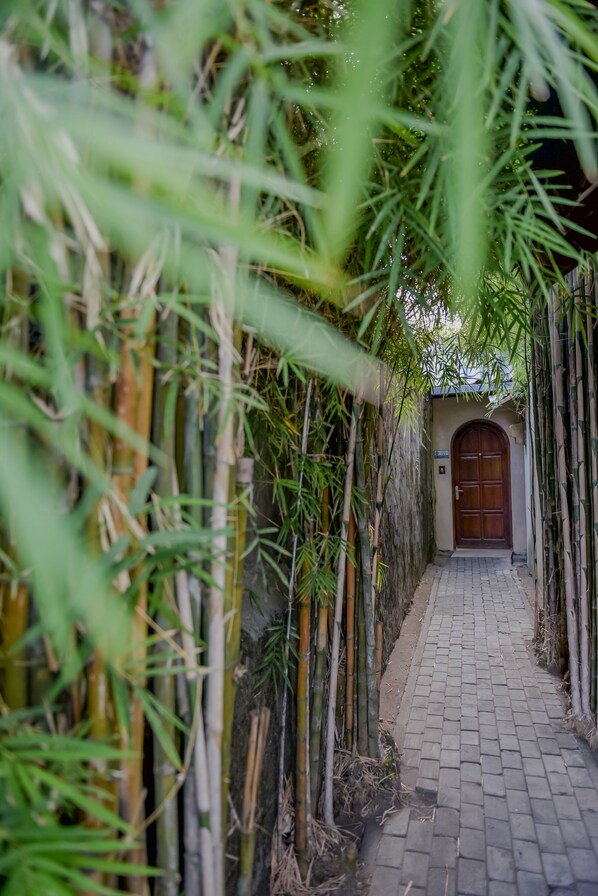 A narrow pathway flanked by bamboo walls leading to a wooden door.