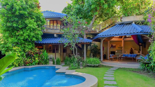 Une piscine entourée d’un jardin bien entretenu, un bâtiment à deux étages doté d’un balcon et un espace salon couvert.