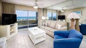 Une chambre d’hôtel avec un balcon, une télévision, un canapé, une table basse et une lampe.
