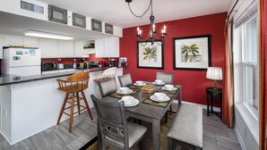 Una cucina moderna con mobili bianchi, un'area pranzo con tavolo apparecchiato per quattro persone e una parete decorata in rosso.