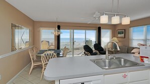 A kitchen with a large island, a dining area with chairs, a ceiling fan, and a view of the ocean through the windows. - Gulf Front, Quiet Beach, Triplex, Indian Pass ~ Pelican Landing 3 (Indian Pass)