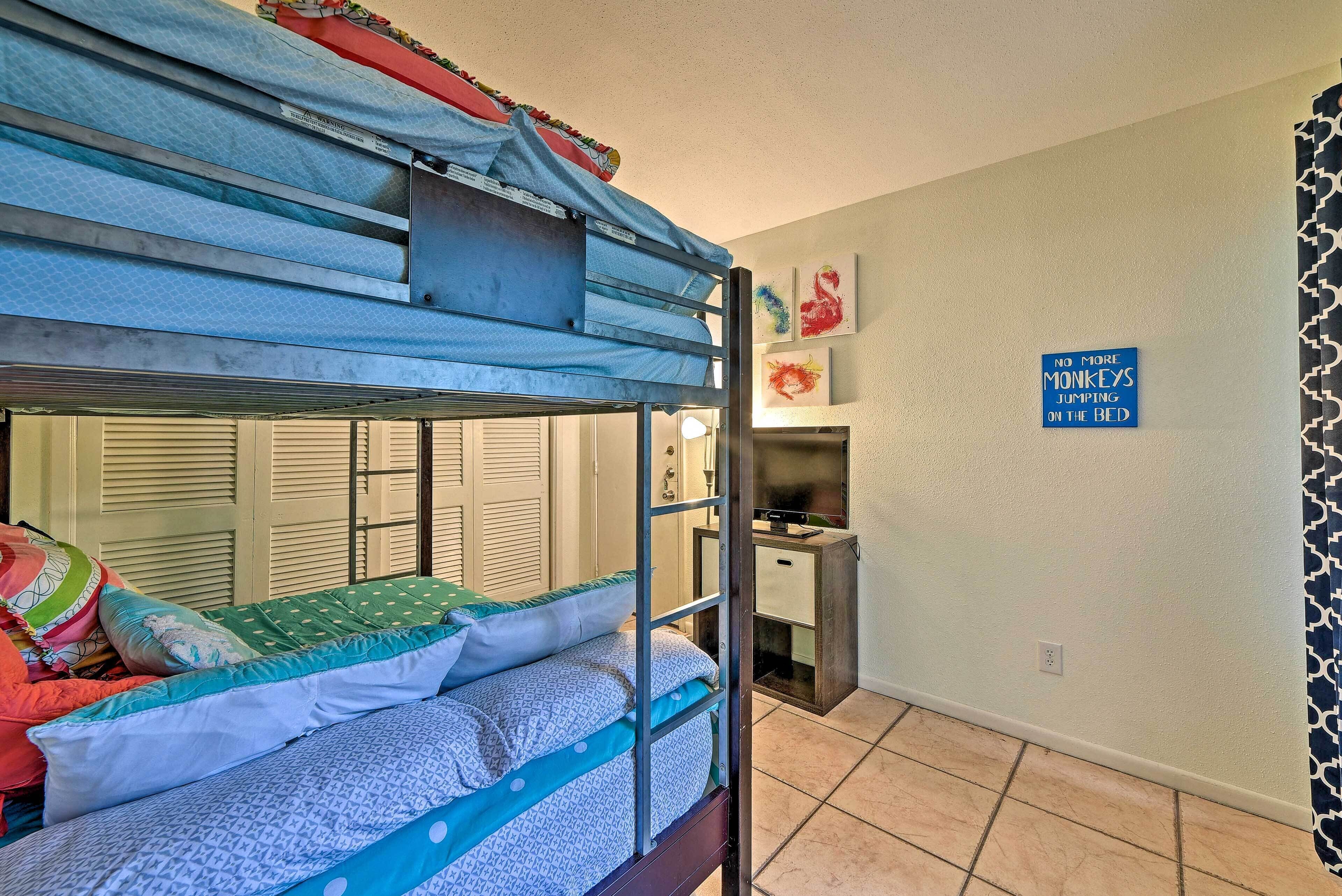 A bunk bed with a ladder, a desk, and a chair in a room with a tiled floor.