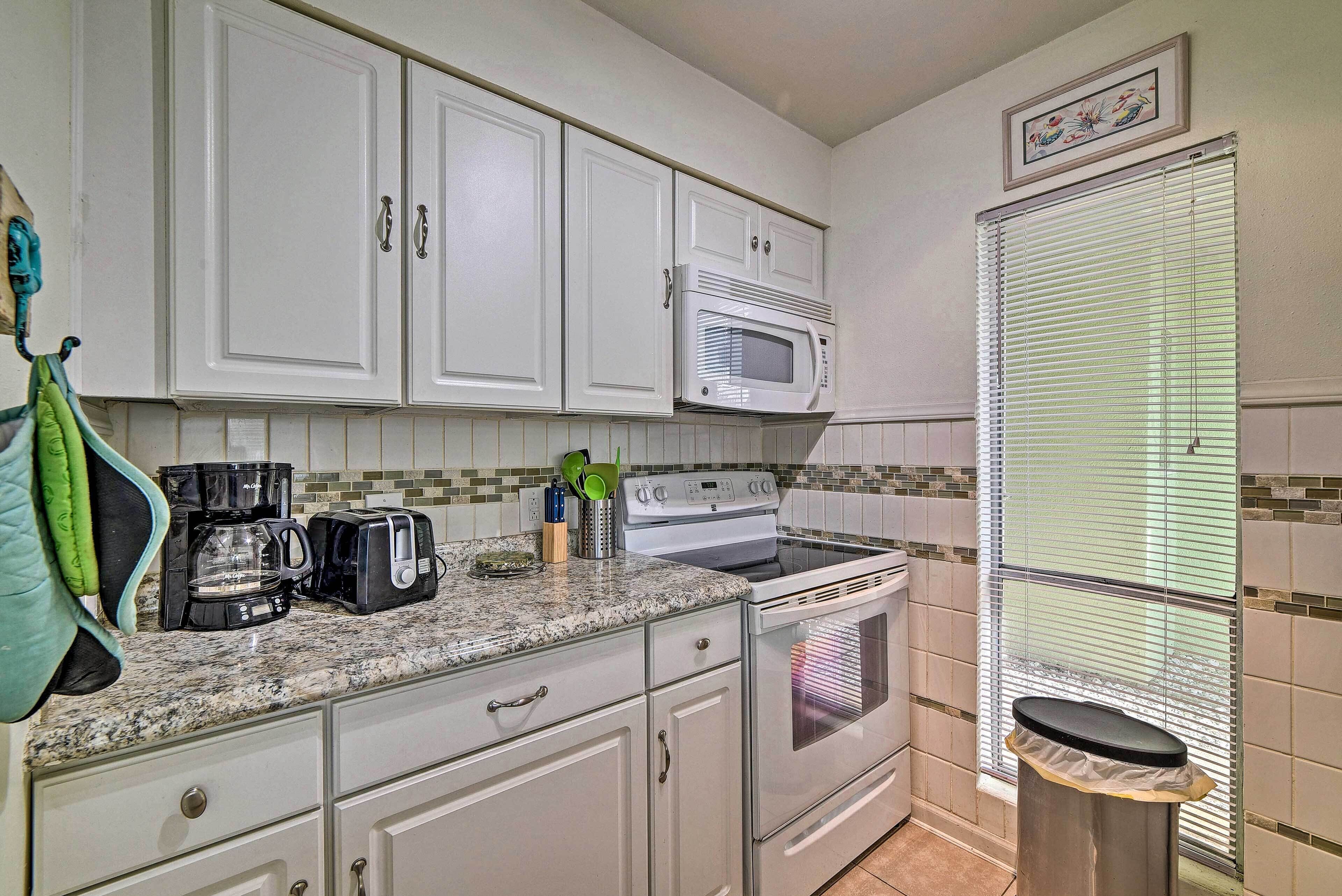 A kitchen with white cabinets, a microwave, a stove, and a trash can.