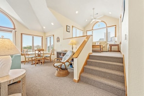 A spacious living area with a staircase, multiple seating options, and large windows.