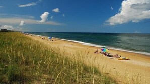 En strand med ett gräsområde, en sandstrand och havet.