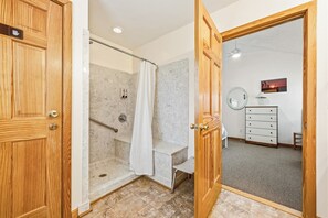 A bathroom with a shower, a vanity with a mirror, and a wooden door. - Blue Heron, Pet Friendly Corolla Home with Private Pool, Hot Tub and Ocean Views! (Corolla)