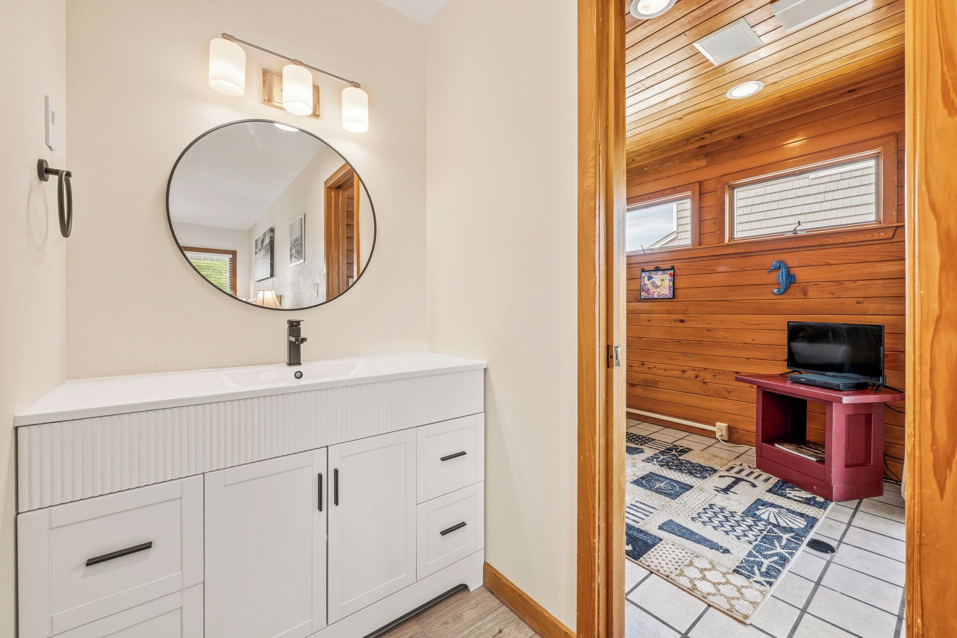 A bathroom with a white vanity, a round mirror, and a wooden ceiling.