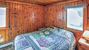 A wooden-paneled room with a bed, a window, and a nightstand with a lamp. - 2 Mi to Boat Ramp! Family Cabin on Long Lake (Hale)