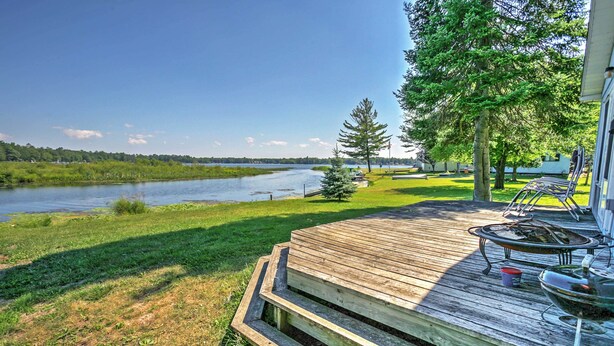 A wooden deck with a fire pit and grill, overlooking a river and a grassy area with trees. - 2 Mi to Boat Ramp! Family Cabin on Long Lake (Hale)