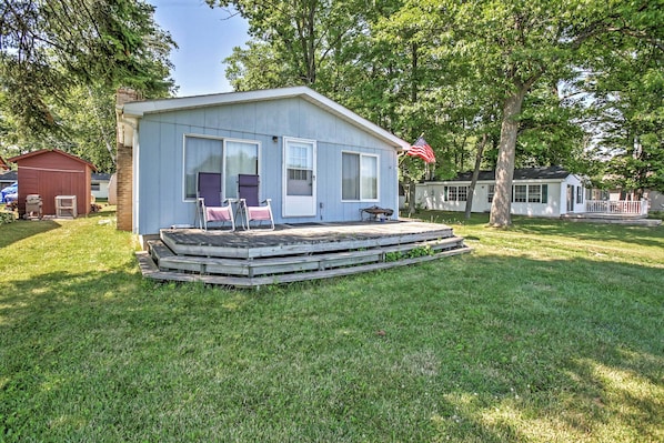 A small, single-story mobile home with a front porch and a flag.
