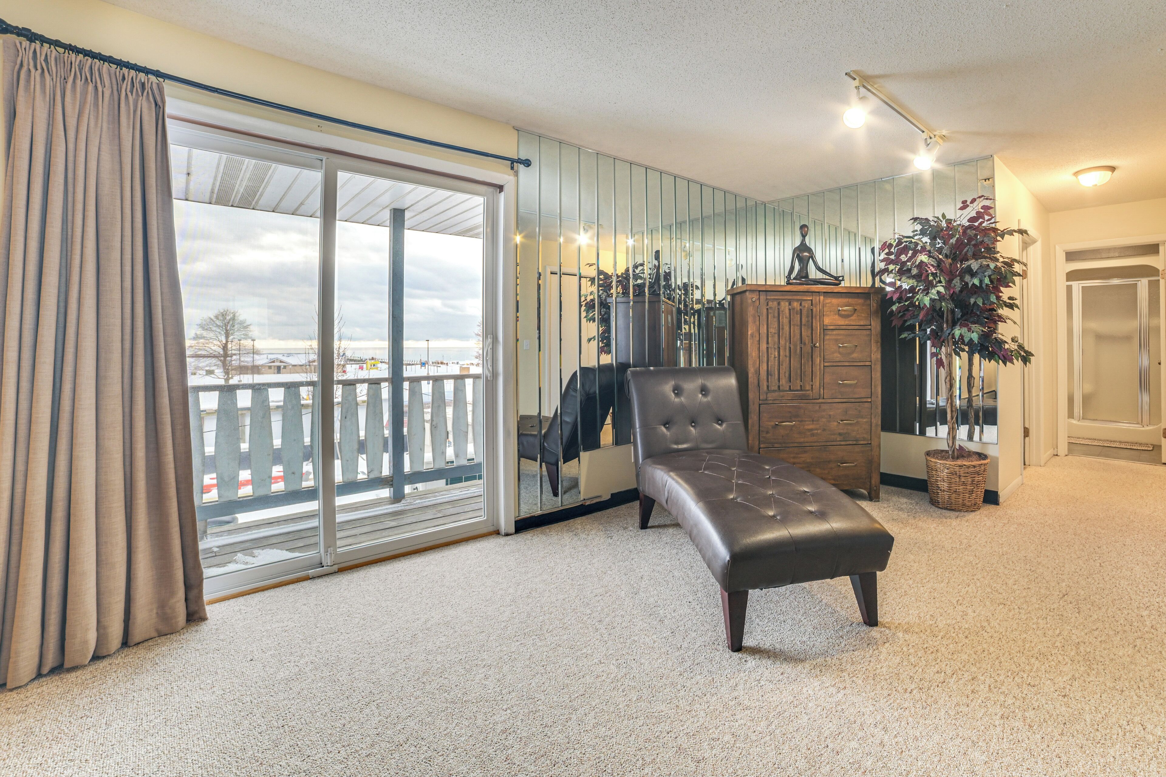 A room with a sliding glass door leading to a balcony, a cushioned bench, a wooden cabinet, and a potted plant.