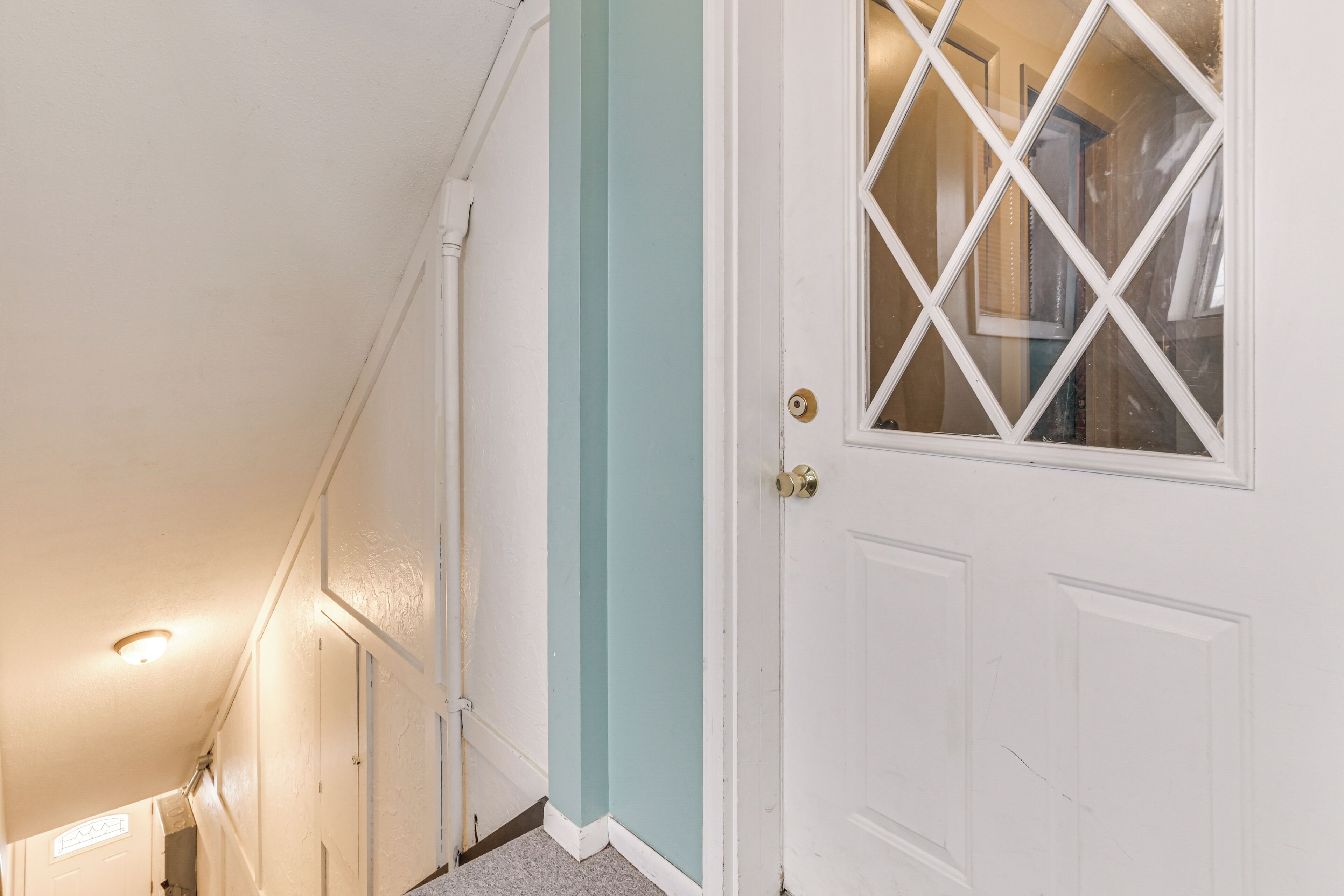 A hallway with a white door with a diamond-patterned window, a teal accent wall, and a white ceiling with a light fixture.