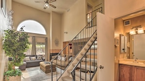 A spacious living room with a large window, a staircase leading to a second floor, a cozy seating area, and a modern bathroom with a large mirror and sink. - Dog-Friendly Tucson Home w/ Patio & Hot Tub (Tucson)