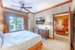 A hotel room with a bed, a ceiling fan, a TV, a desk with drawers, and a view of the outdoors through a window.