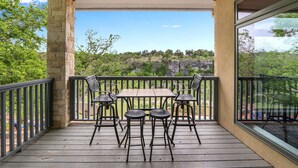A balcony with a table and chairs, overlooking a natural landscape. - Rio Cantando I Blanco River, Pool, Hot Tub, Game Room (Wimberley)