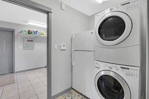 A laundry room with two stacked washing machines, a tiled floor, and a door leading to another room. - Rio Cantando I Blanco River, Pool, Hot Tub, Game Room (Wimberley)