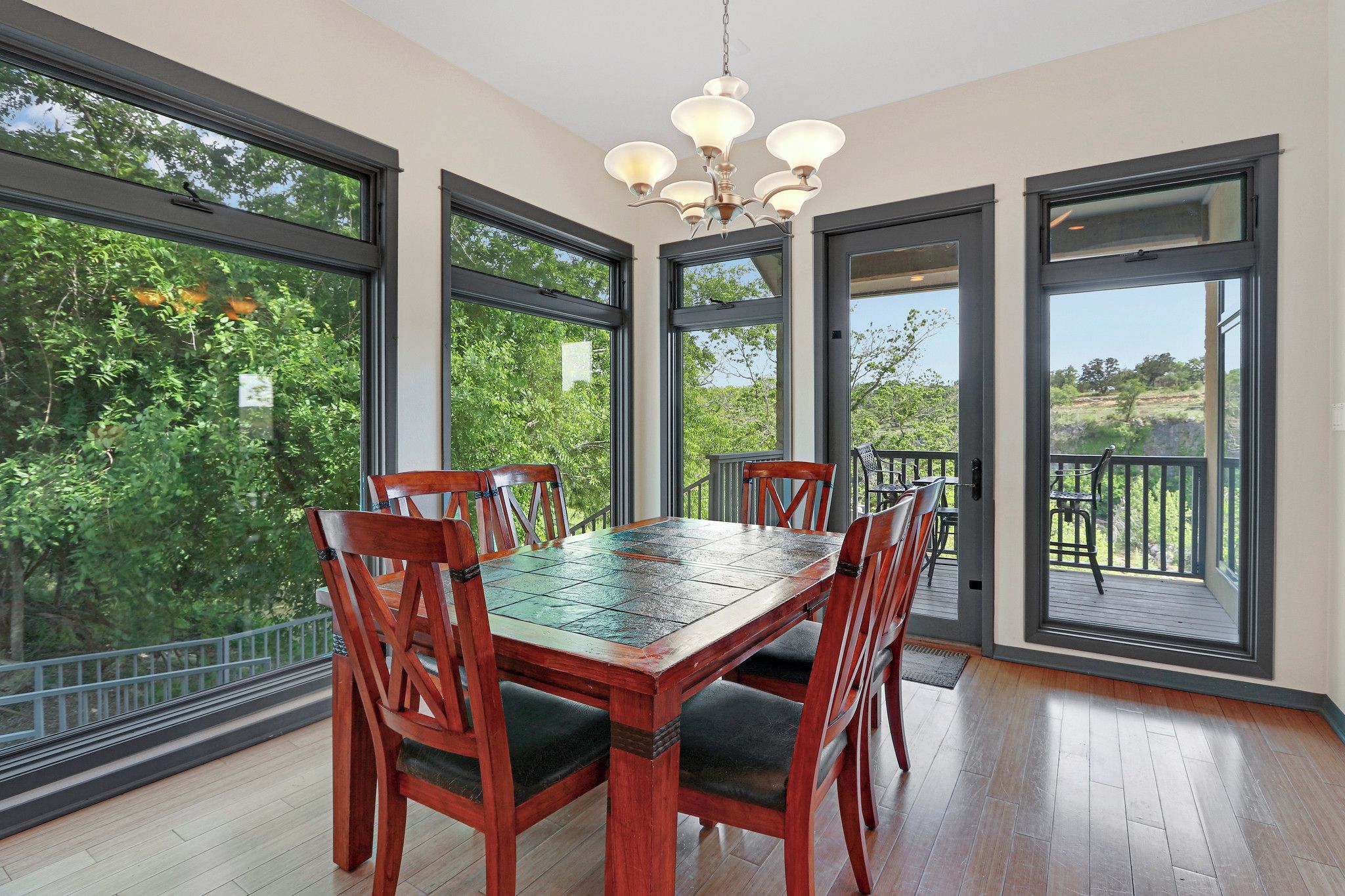 A dining area with a wooden table and chairs, large windows, and a view of greenery.