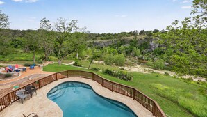 A swimming pool with a wooden deck and chairs, surrounded by a grassy area and trees. - Rio Cantando I Blanco River, Pool, Hot Tub, Game Room (Wimberley)