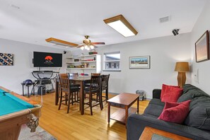 A living room with a pool table, a dining area with chairs, a sofa with cushions, a TV mounted on the wall, and a ceiling fan. - Rio Cantando I Blanco River, Pool, Hot Tub, Game Room (Wimberley)