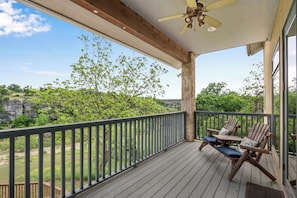 A wooden deck with a table and chairs, overlooking a natural landscape. - Rio Cantando I Blanco River, Pool, Hot Tub, Game Room (Wimberley)
