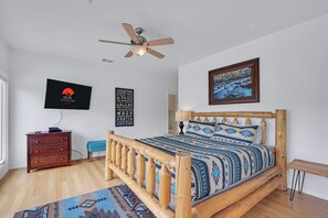 A bedroom with a wooden bed, a ceiling fan, a television, a framed picture, and a wall with city names.