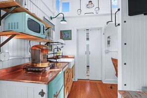 A compact kitchen with a vintage microwave, coffee machine, and wooden cabinets. - Chic Caboose in Wimberley Square (Wimberley)