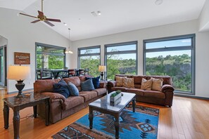 A spacious living room with a ceiling fan, large windows, and a dining area with a table and chairs.