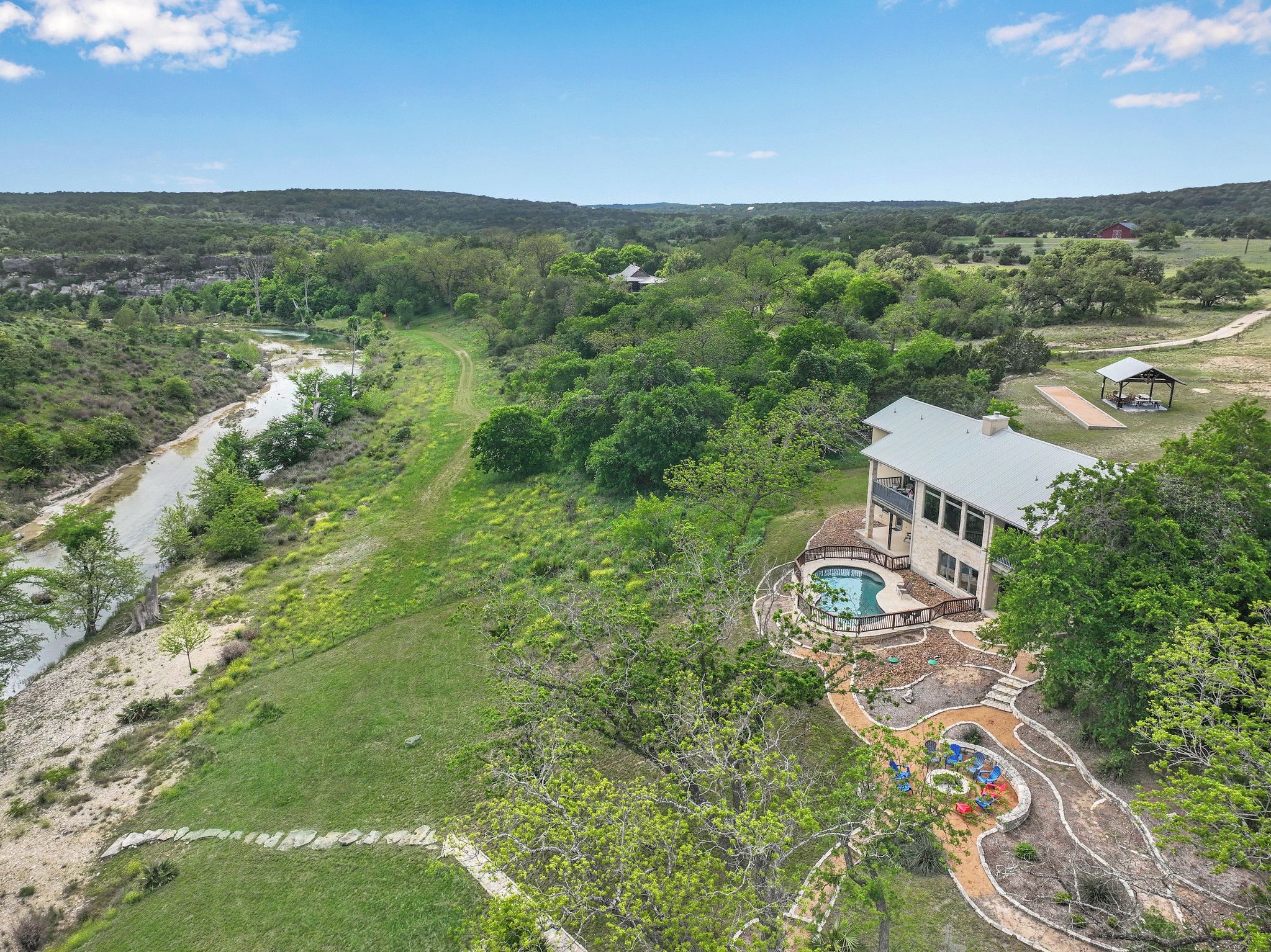 A house with a swimming pool, surrounded by a lush landscape and a river.