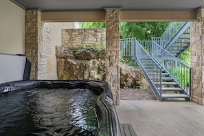 A hot tub in a covered outdoor area with stone walls and a staircase leading to a balcony. - Rio Cantando I Blanco River, Pool, Hot Tub, Game Room (Wimberley)
