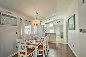 A dining area with a wooden table set for four, white chairs, and a hanging light fixture. - Beachy Lavallette Cottage w/ Outdoor Shower, Patio (Lavallette)