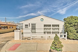 A small, single-story building with a white exterior, a small porch, and a decorative sailboat sign on the roof. - Beachy Lavallette Cottage w/ Outdoor Shower, Patio (Lavallette)