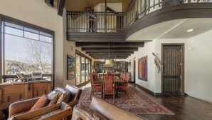 A spacious interior with a dining area, a loft with a balcony, and a large window offering a view. - Stunning Mountain Home by InvitedHome | Hot Tub, Game Room, Golf Course, Hiking (Mountain Village)