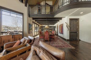 A spacious interior with a dining area, a loft with a balcony, and a large window offering a view. - Stunning Mountain Home by InvitedHome | Hot Tub, Game Room, Golf Course, Hiking (Mountain Village)