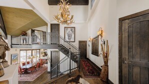 A spacious interior with a staircase, a chandelier, a dining area, and a large wooden door. - Stunning Mountain Home by InvitedHome | Hot Tub, Game Room, Golf Course, Hiking (Mountain Village)