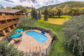 A pool area with a wooden deck, lounge chairs, and a view of a golf course. - All Seasons 104 at Park City Mountain (Park City)