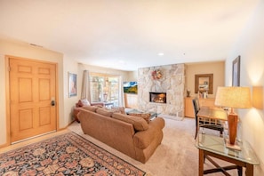 A living room with a sofa, a glass coffee table, a fireplace, and a dining area with a table and chairs. - All Seasons 104 at Park City Mountain (Park City)