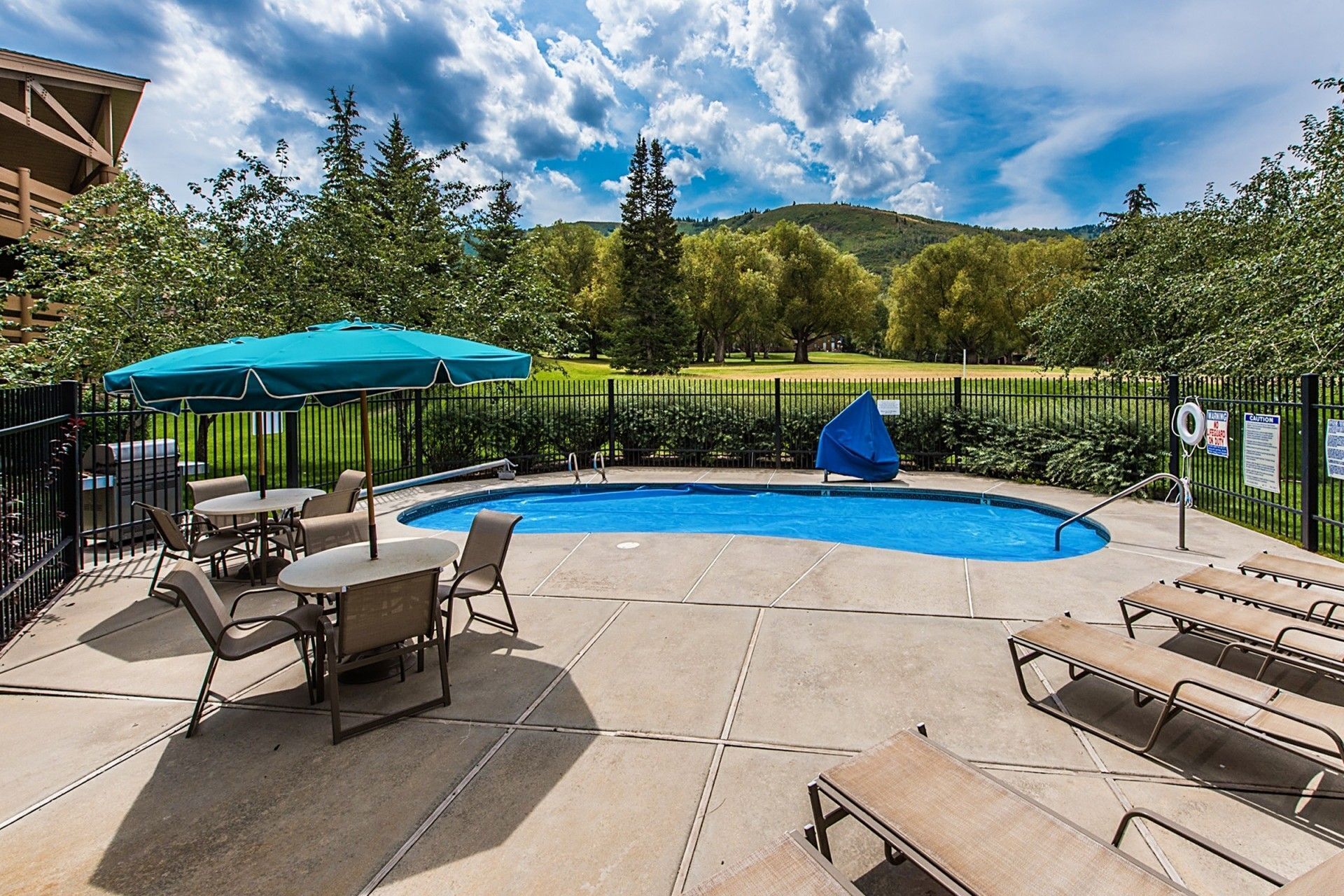 A backyard with a swimming pool, lounge chairs, and a covered patio area.